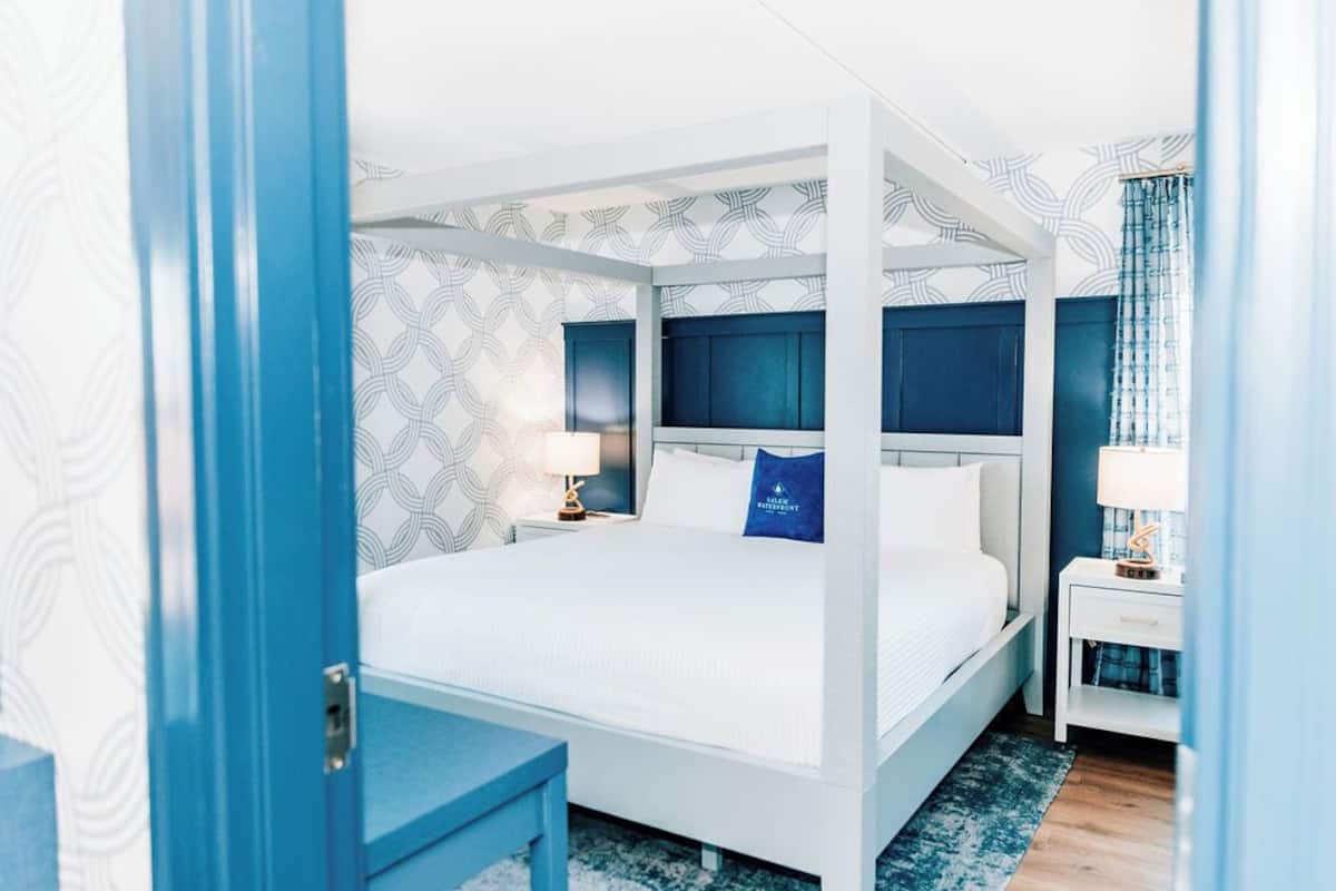 Una cama con dosel con una decoración en blanco y azul, una mesita de noche con lámpara y un papel tapiz estampado.