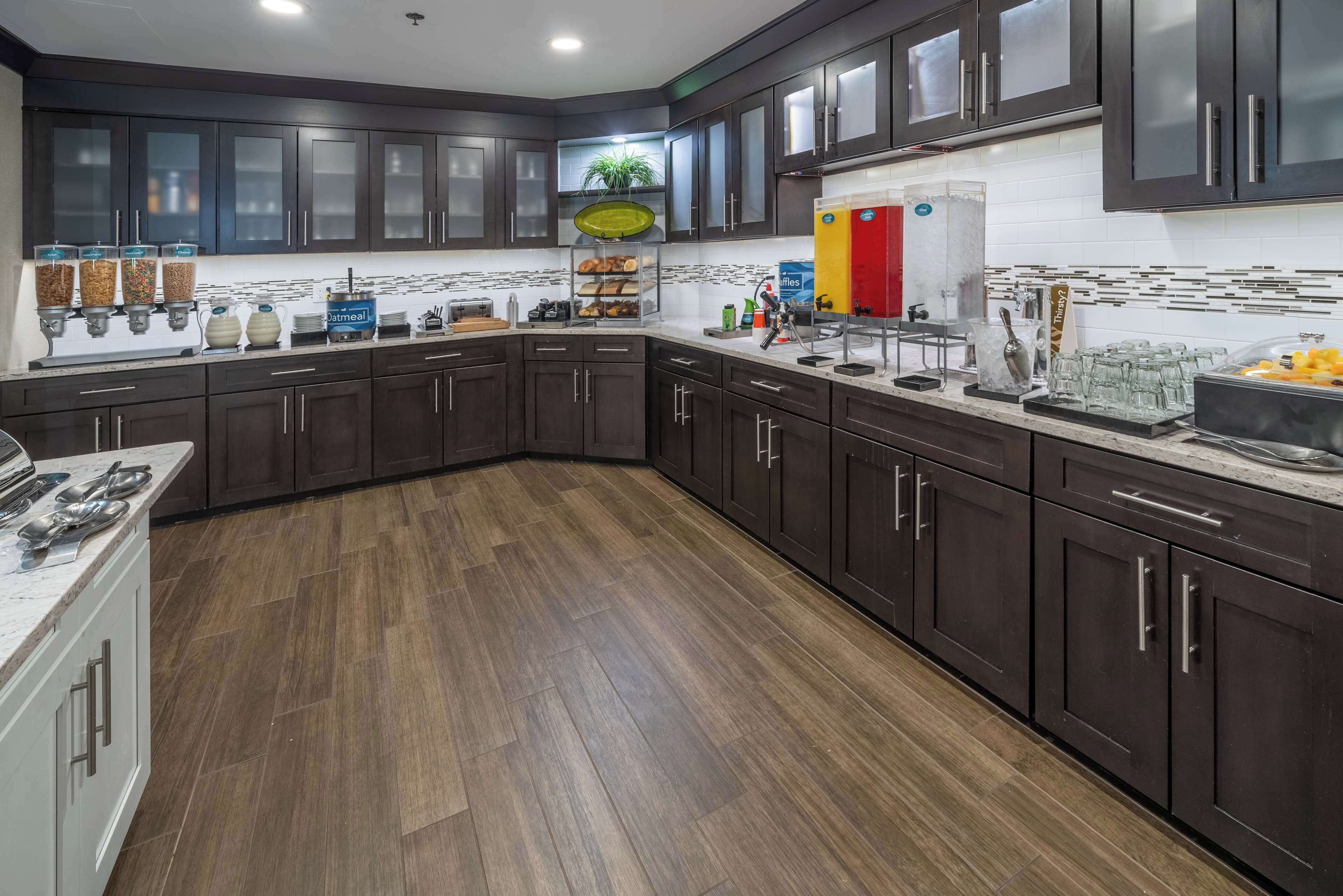 A modern kitchen with dark wood cabinets, a white tiled backsplash, and a wooden floor.