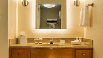 A hotel bathroom with a wooden vanity, two wall-mounted lights, a mirror, and a towel rack.