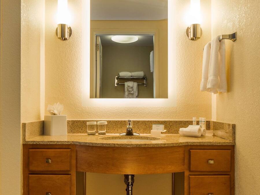 A hotel bathroom with a wooden vanity, two wall-mounted lights, a mirror, and a towel rack.