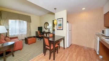Una habitación de hotel compacta con comedor, sofá, una mesita y una zona de cocina.