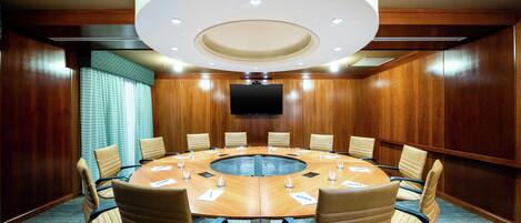 A conference room with a round table, 12 chairs, and a flat-screen TV mounted on the wall.