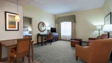 Une chambre d’hôtel avec un bureau en bois, une chaise, un canapé, une télévision, un miroir et un tableau encadré au mur.