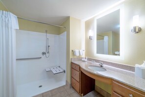 Un baño con ducha, lavamanos, espejo y toallero.