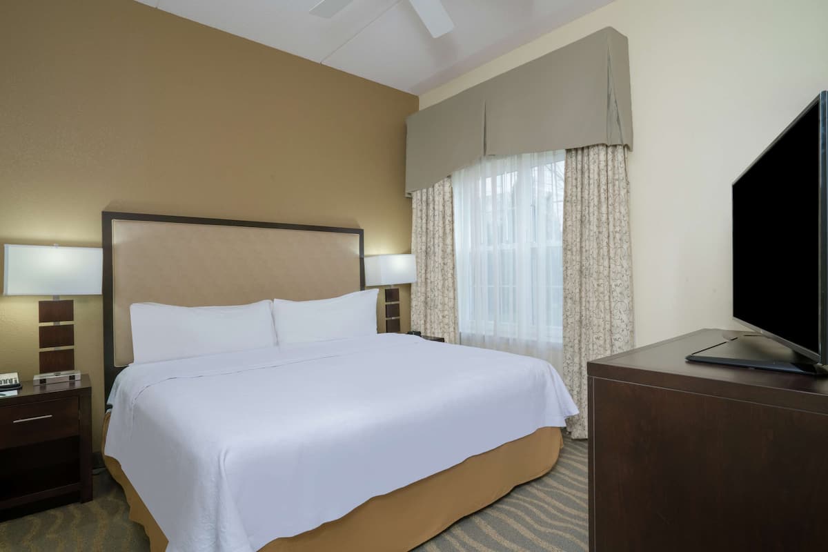 Ein Hotelzimmer mit einem großen Bett, einem Schreibtisch mit Fernseher und einem Fenster mit Vorhängen.