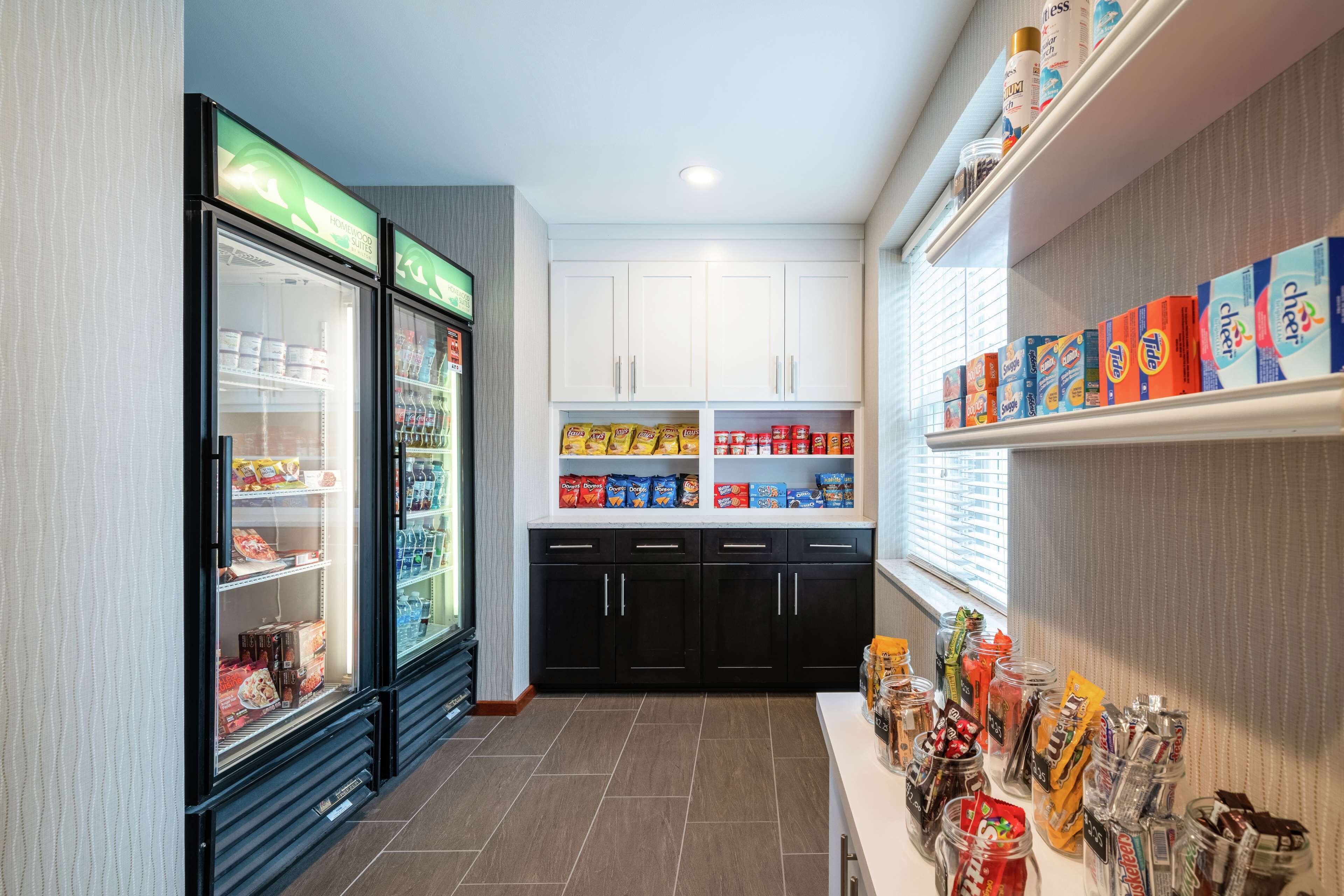 A kitchenette with a refrigerator, pantry, and shelves stocked with snacks and condiments.