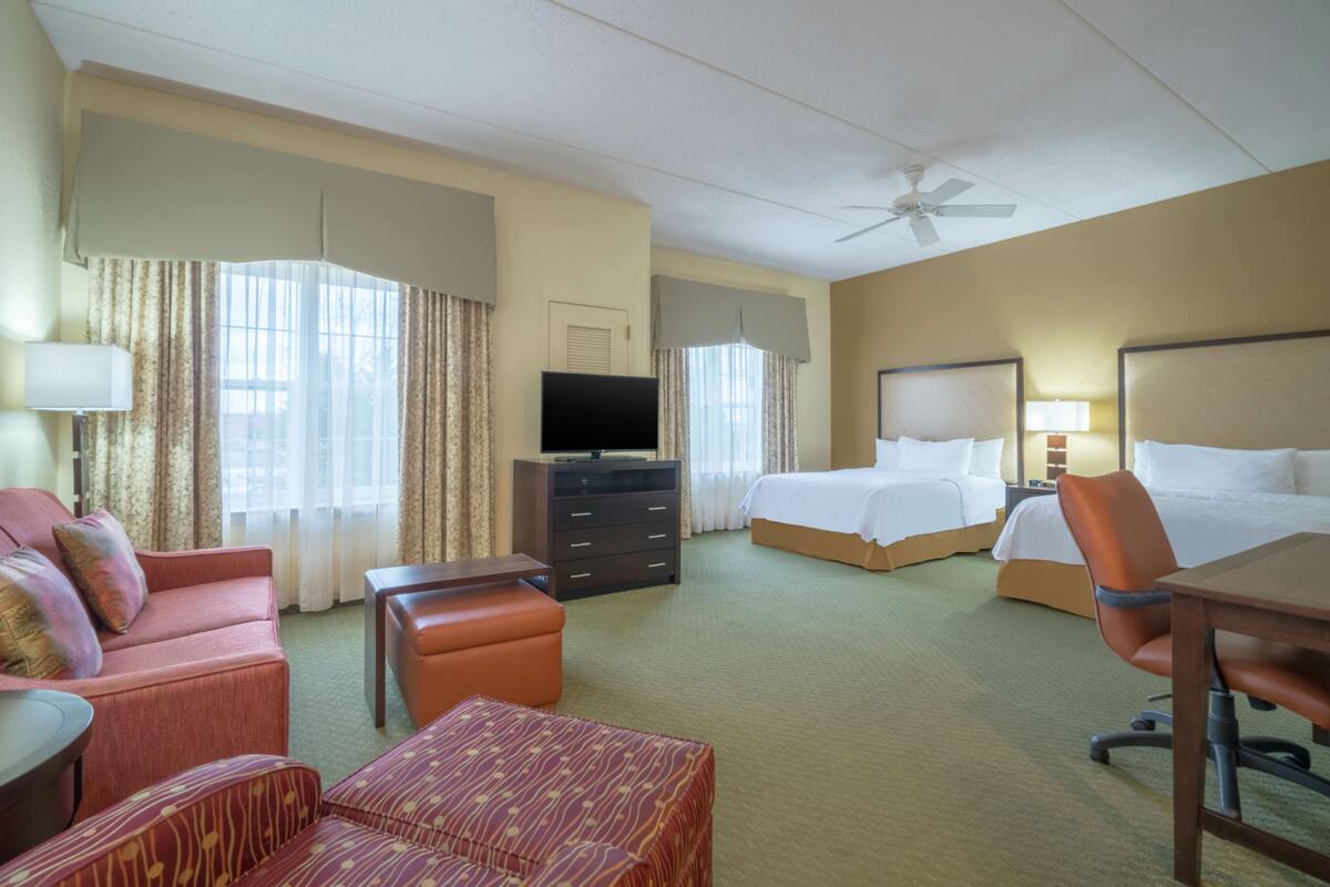 Ein Hotelzimmer mit einem Bett, einem Schreibtisch, einem Stuhl, einem Fernseher und einem Deckenventilator.