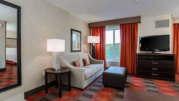 Una habitación de hotel con sofá, televisión, lámpara y ventana con cortinas.
