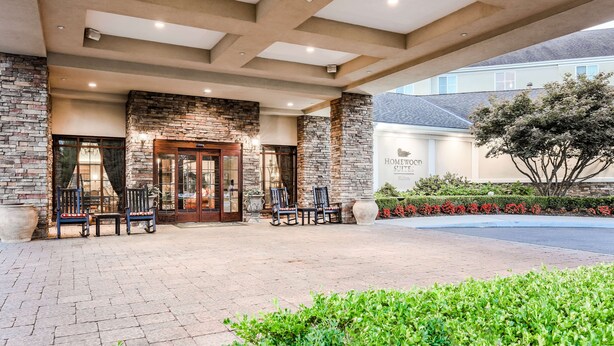 A hotel entrance with stone walls, a covered patio, and outdoor seating. - Homewood Suites Melville (Melville)