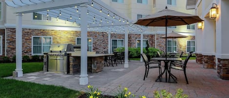 An outdoor patio with a grill, seating, and string lights.