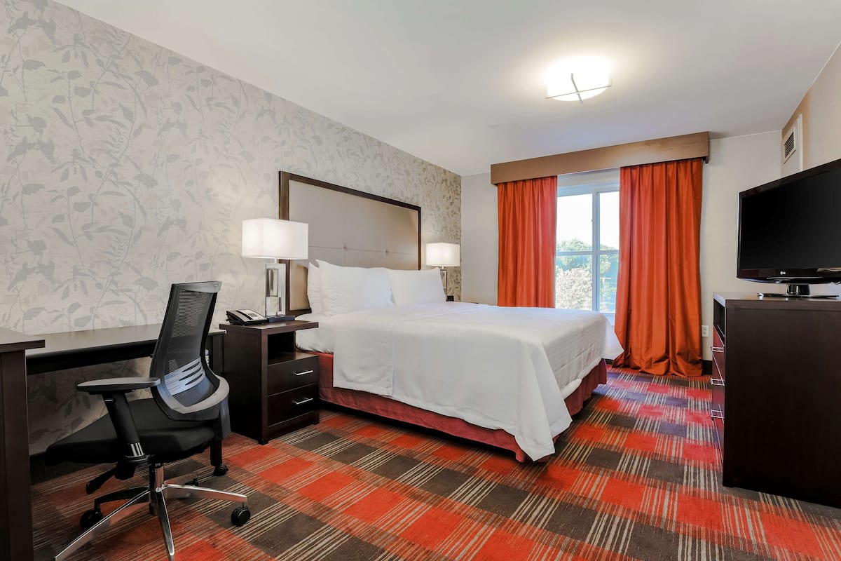 A hotel room with a bed, desk, chair, television, and a window with curtains.