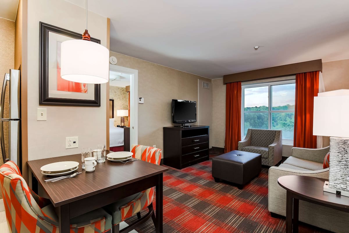A hotel room with a dining table set, a sofa, a TV, and a window with curtains.
