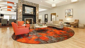 A spacious living room with a fireplace, modern furniture, and a large rug. - Homewood Suites Melville (Melville)