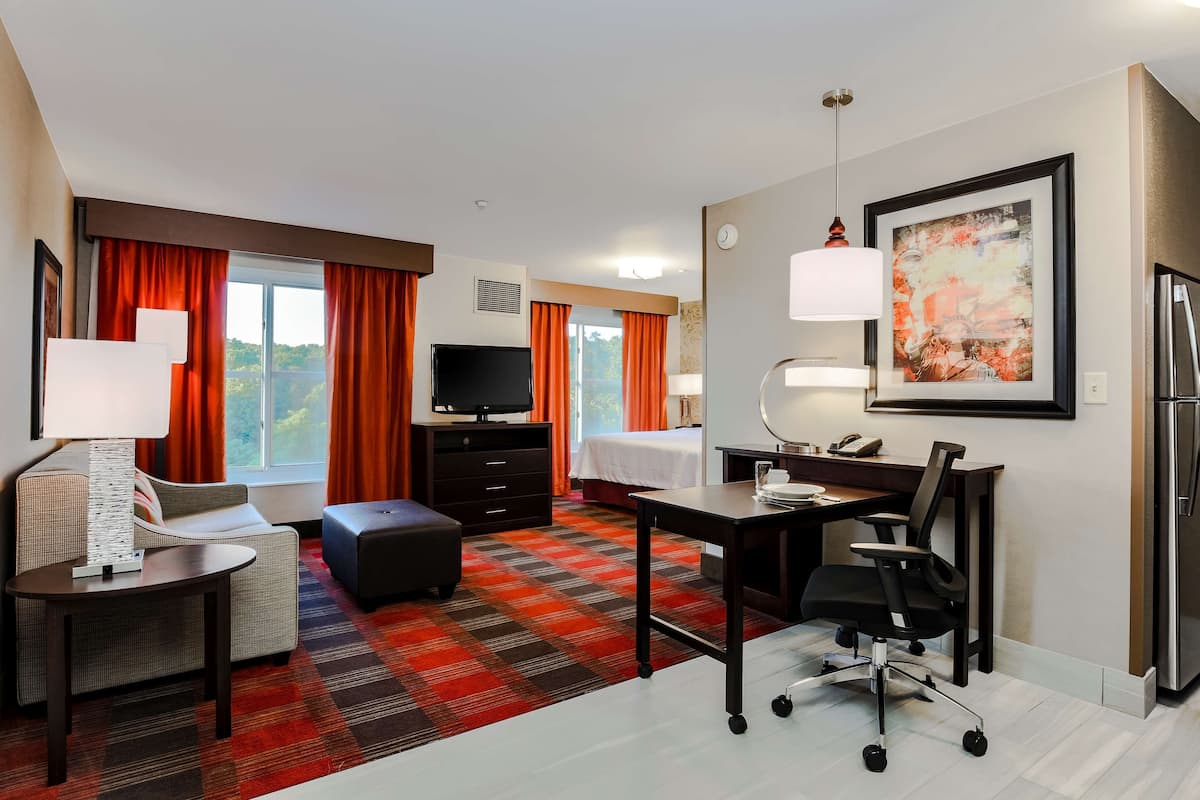 A hotel room with a bed, a desk, a chair, a TV, a lamp, and a refrigerator.