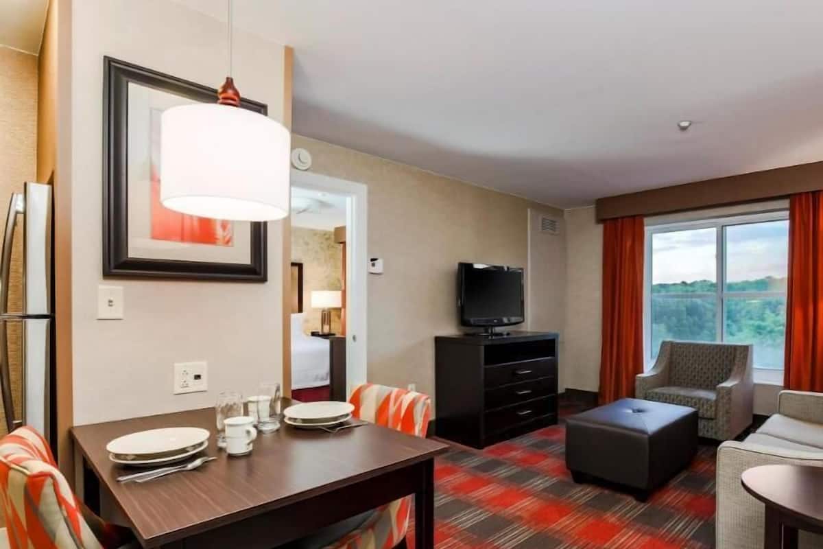 A hotel room with a dining table, chairs, a sofa, a TV, and a large window.
