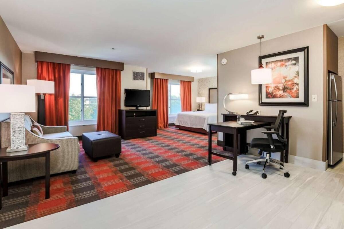 A hotel room with a bed, a desk, a chair, a television, a lamp, and a painting on the wall.