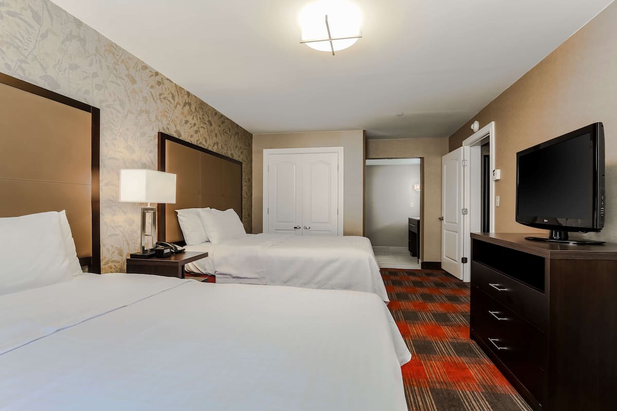 A hotel room with two beds, a TV, a desk with a lamp, and a wardrobe.