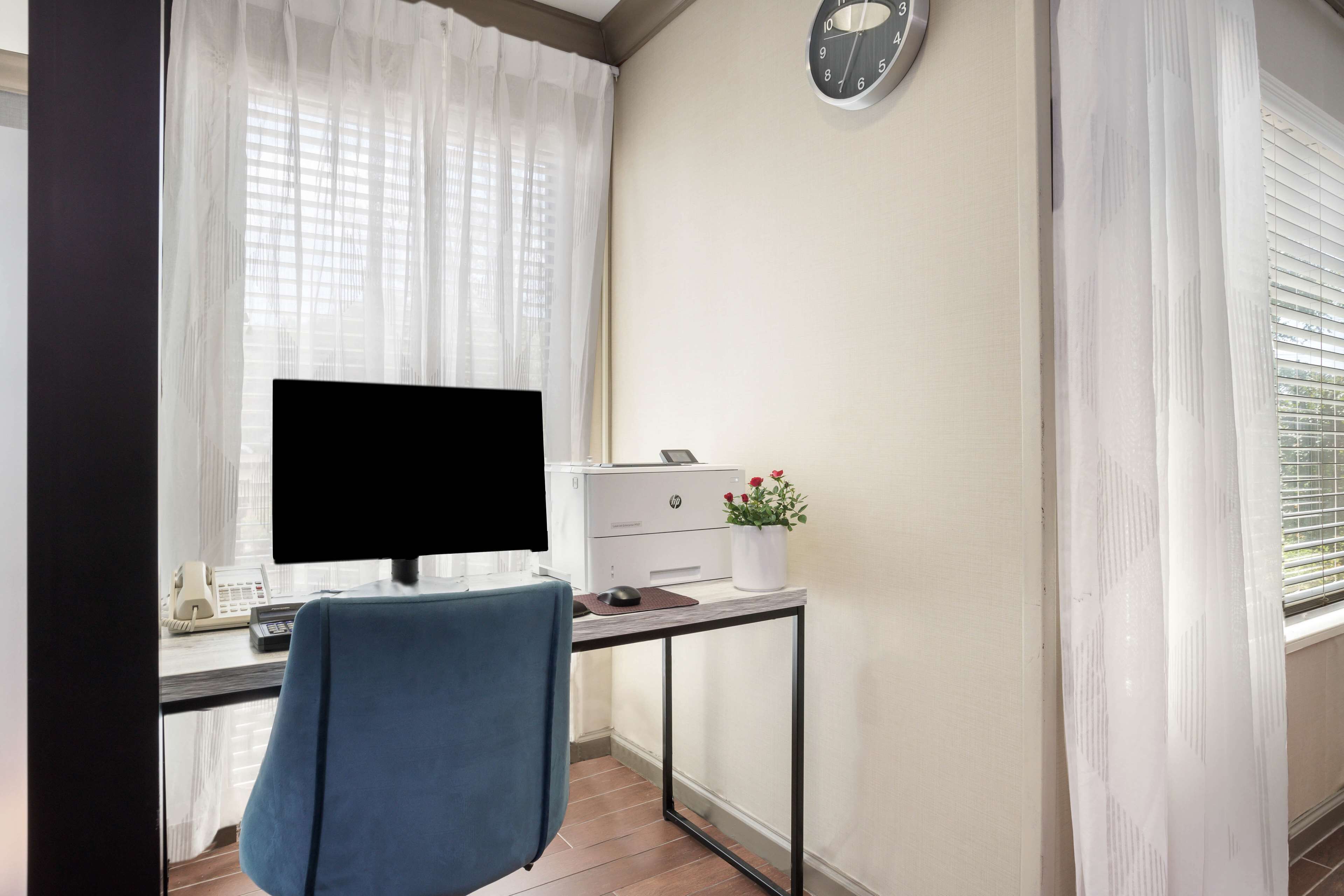 A small office space with a desk, computer, printer, and a clock on the wall.