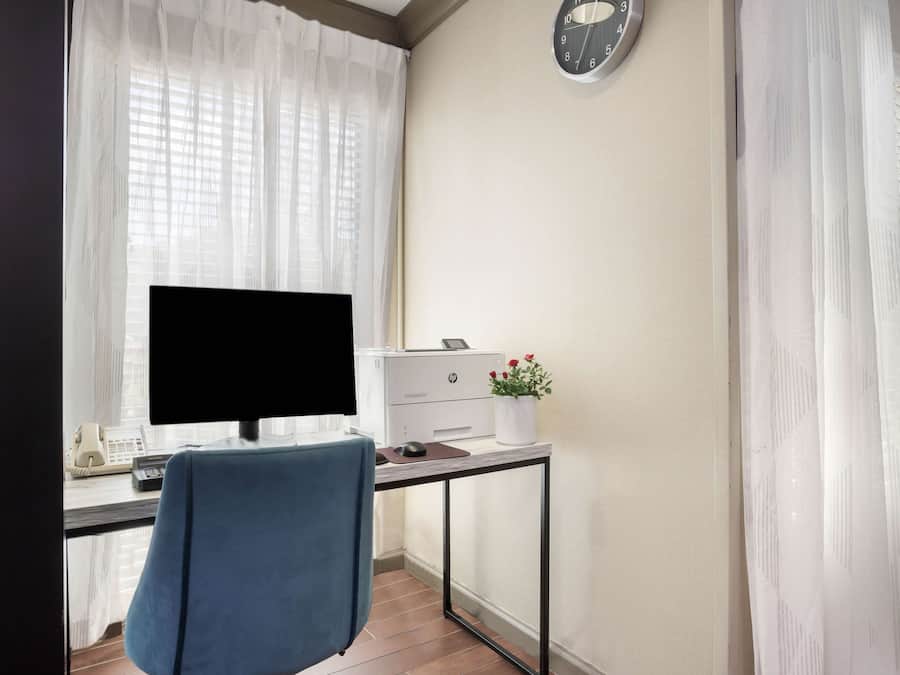 A small office space with a desk, computer, printer, and a clock on the wall.