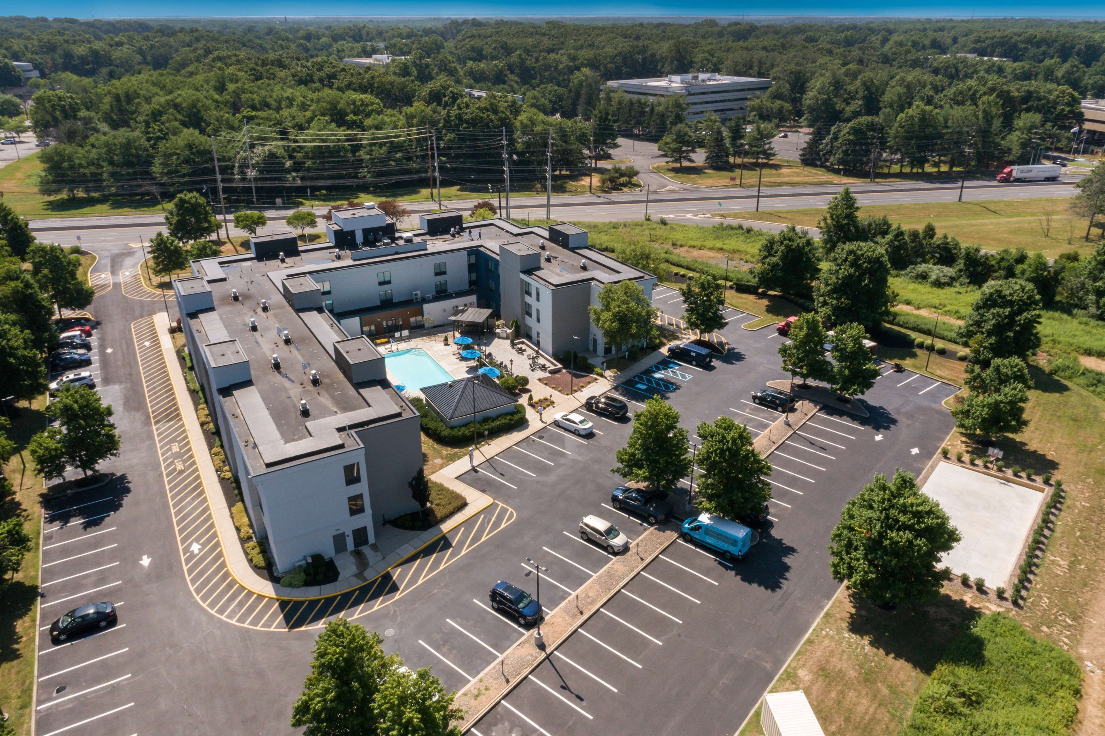An aerial view of a parking lot with multiple buildings, including a swimming pool area, surrounded by greenery and trees.