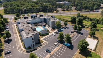 An aerial view of a parking lot with multiple buildings, including a swimming pool area, surrounded by greenery and trees.