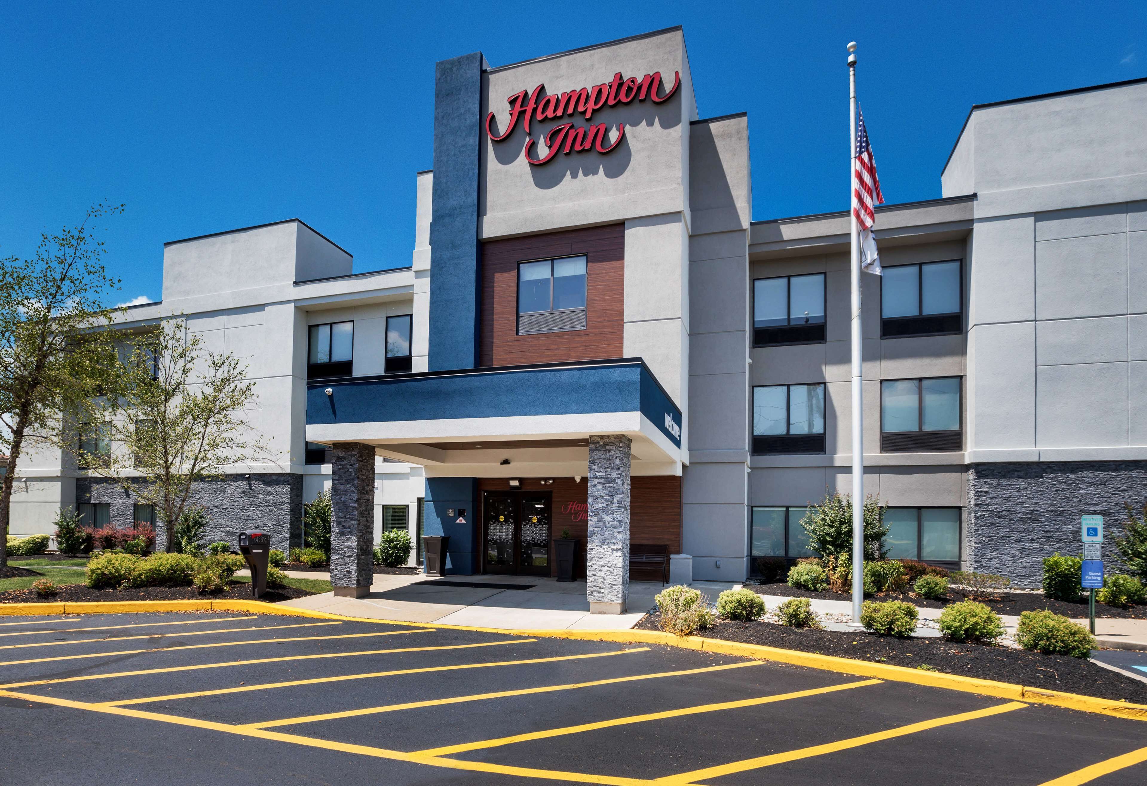 A Hampton Inn hotel with a modern facade, a parking lot, and an American flag.