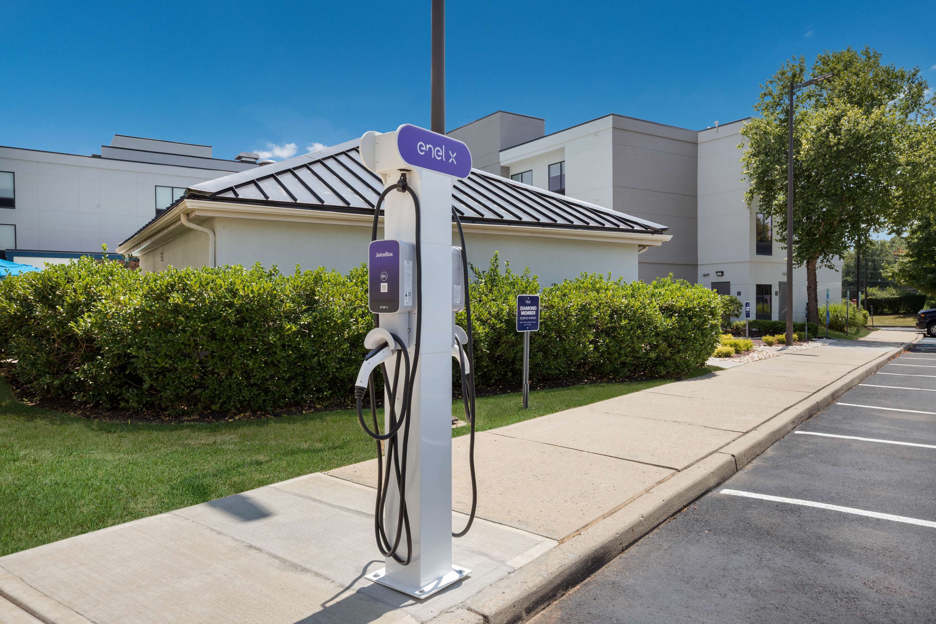 An electric vehicle charging station with a clear sky and modern buildings in the background.