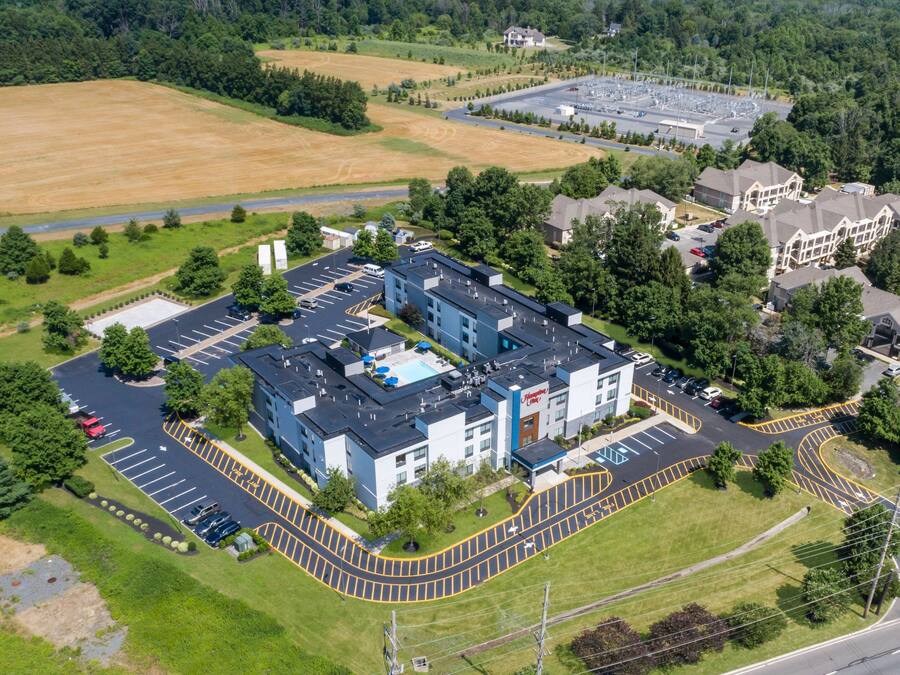 An aerial view of a hotel with a parking lot, a swimming pool, and a large building with multiple units.