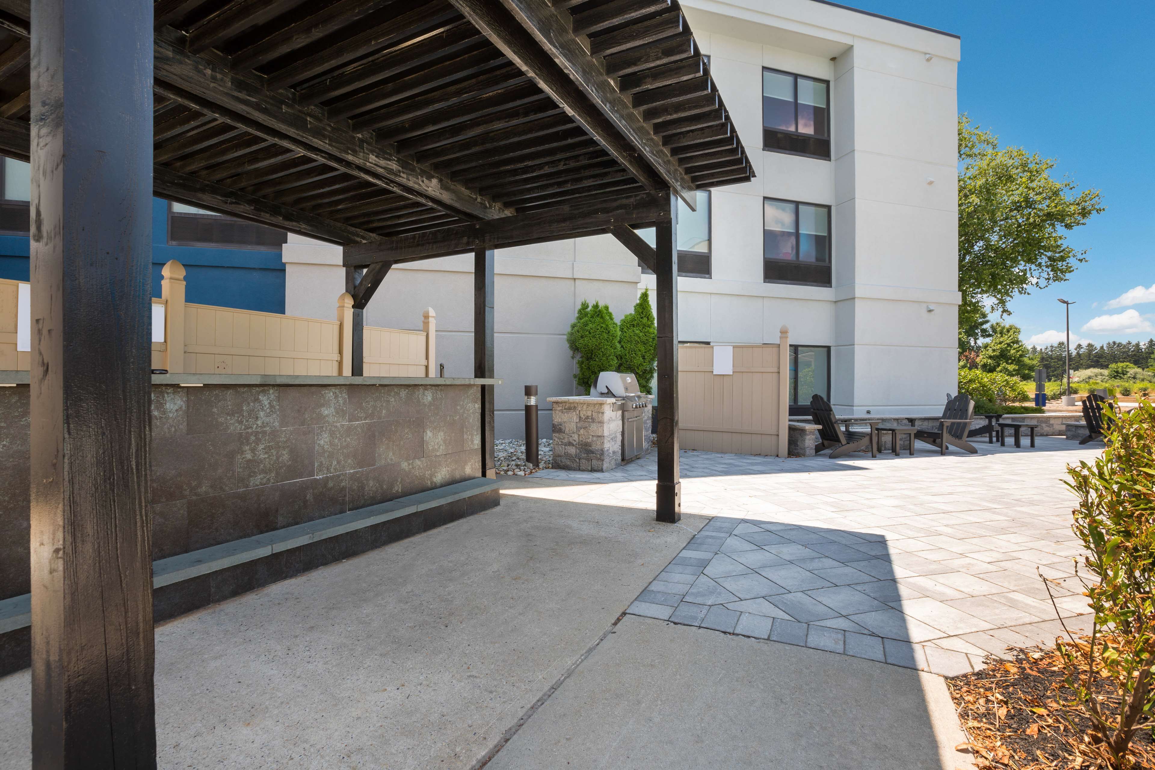 An outdoor patio area with a covered seating area, a stone wall, and a building in the background.