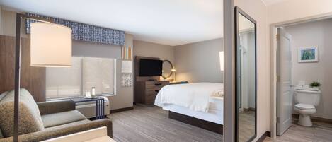 Una habitación de hotel con sofá, cama, televisor, escritorio y baño.