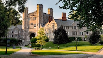 A large, historic building with a prominent entrance, multiple towers, and a well-maintained lawn.