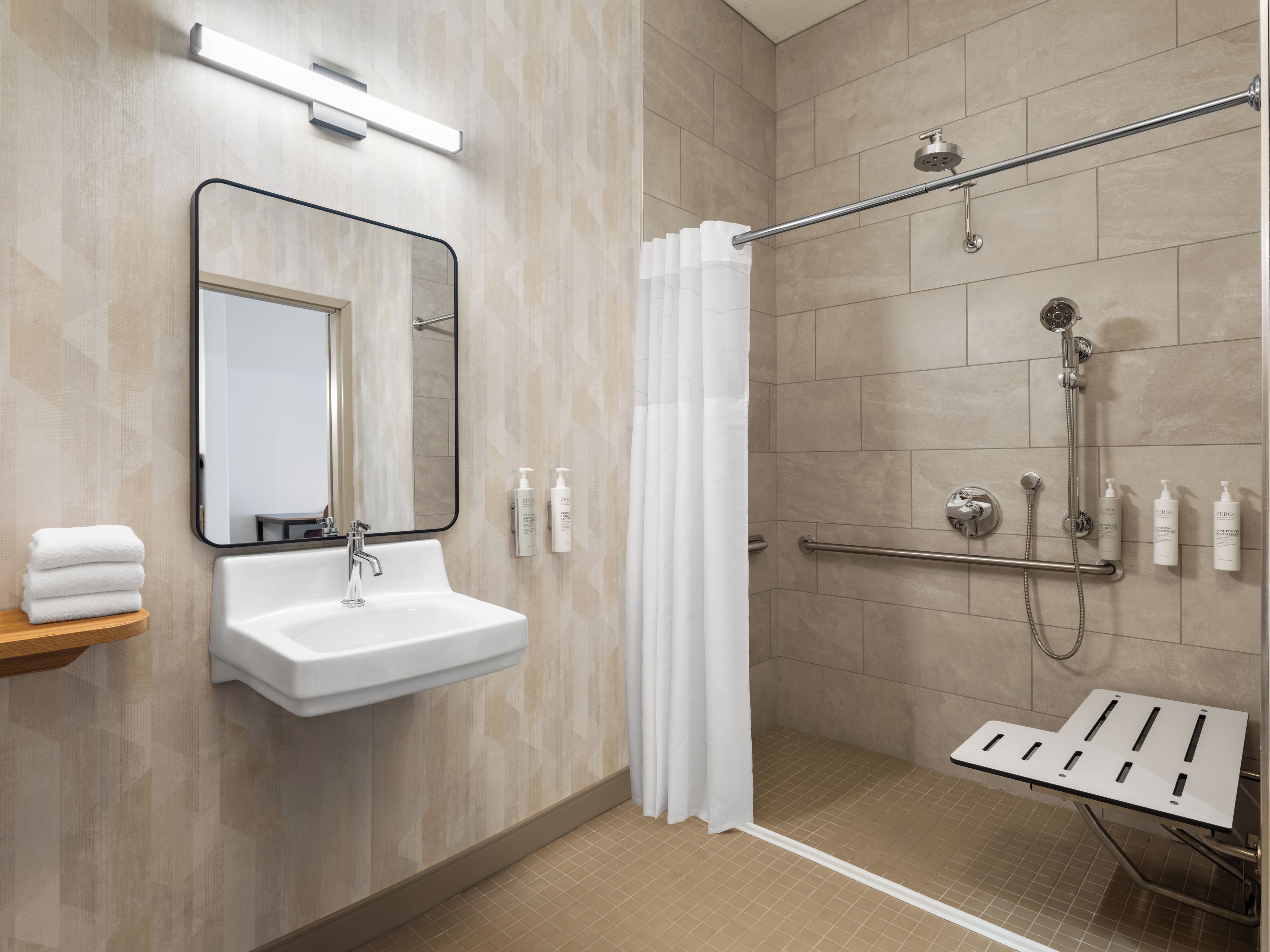 A modern bathroom with a sink, mirror, shower, and handrails.