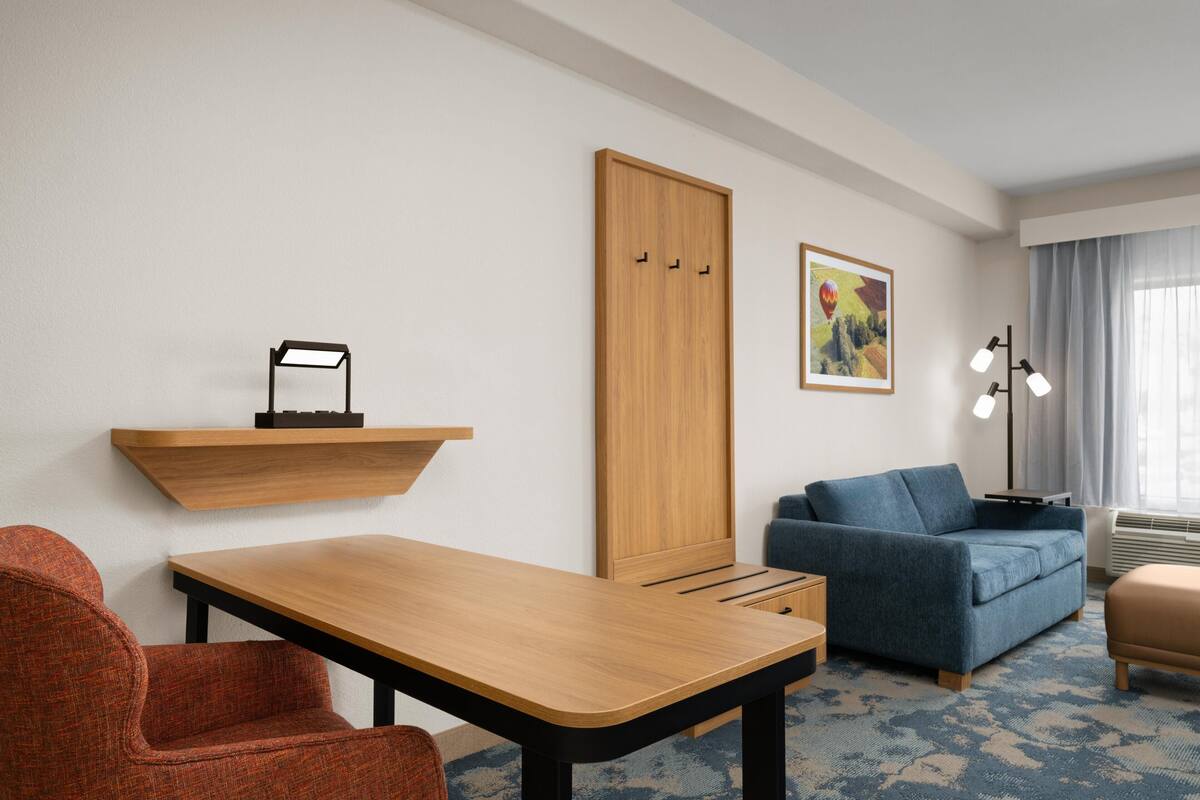 A hotel room with a wooden desk, a blue sofa, a red chair, a wardrobe, and a painting on the wall.