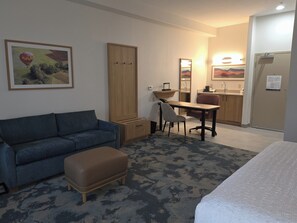 A hotel room with a sofa, a desk, a chair, a small table, a cabinet, and a bed. - Hampton Inn & Suites Ontario (Ontario)