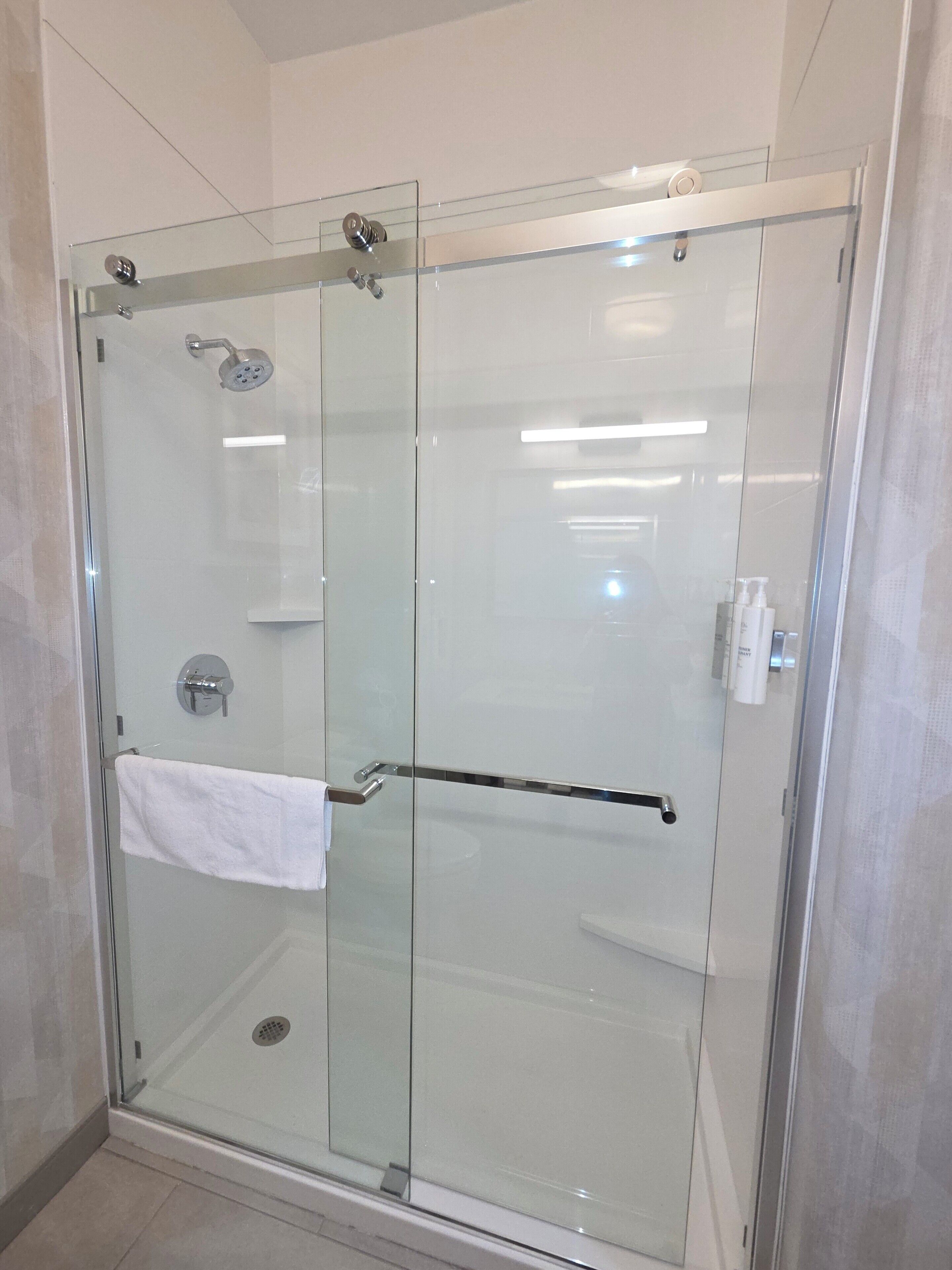 Une douche fermée par des parois en verre, avec un porte-serviettes et un sèche-mains.