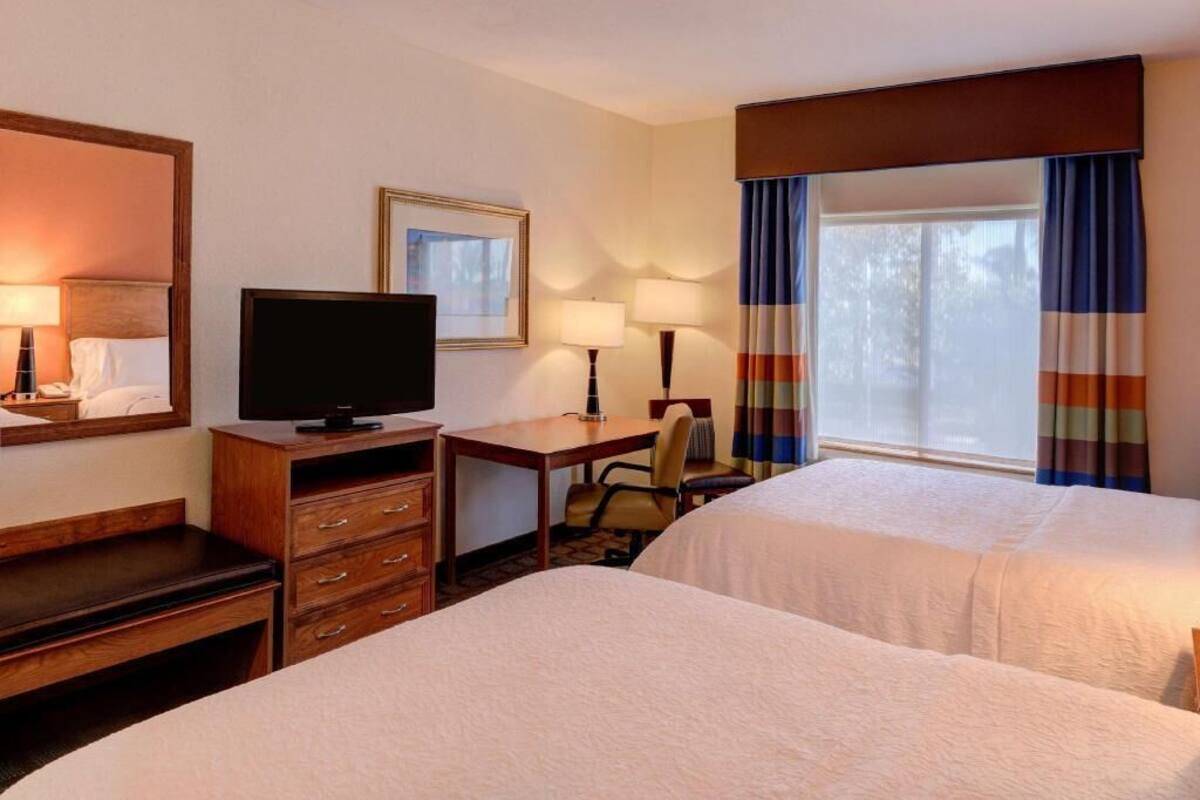 A hotel room with two beds, a desk, a television, a chair, and a window with curtains.