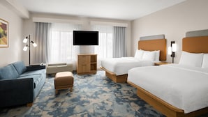 Quarto de hotel com duas camas, um sofá, uma televisão e uma escrivaninha.
