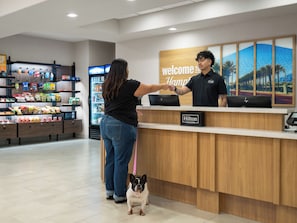 A hotel reception area with a wooden counter, a digital screen displaying the hotel's name, and a wall with a tropical mural.