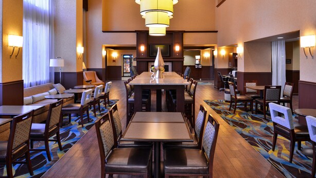 Uma sala de jantar de hotel com uma mesa comprida, várias cadeiras e um tapete estampado.