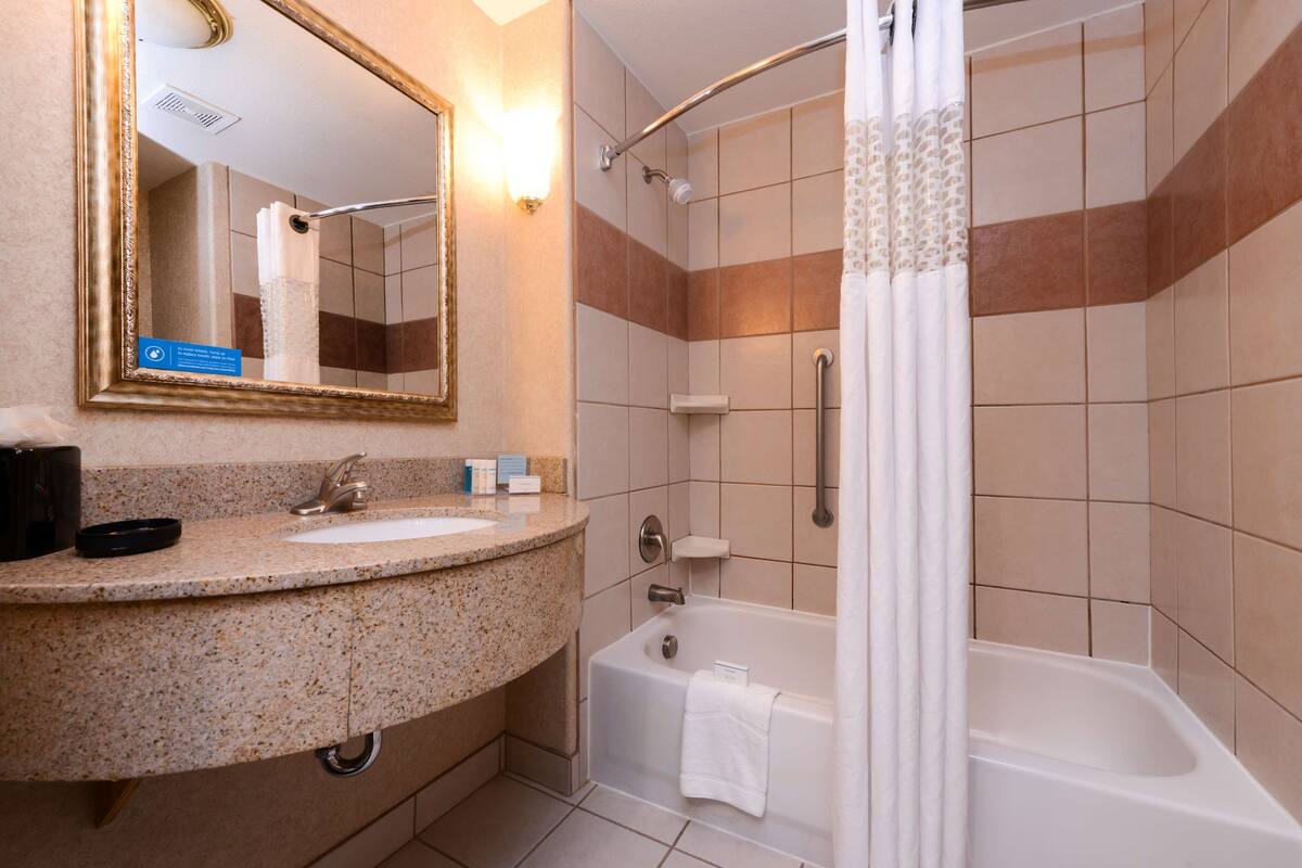A bathroom with a granite countertop sink, a white bathtub, and a shower with a glass door.