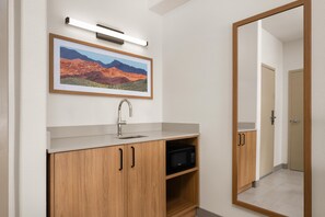 Une salle de bain avec un meuble-lavabo en bois, un évier, un tableau représentant un paysage encadré et un miroir.