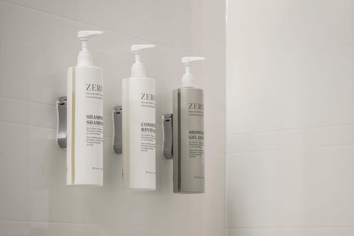 Three ZERO brand bathroom products: shampoo, conditioner, and shower gel, mounted on a white tiled wall.