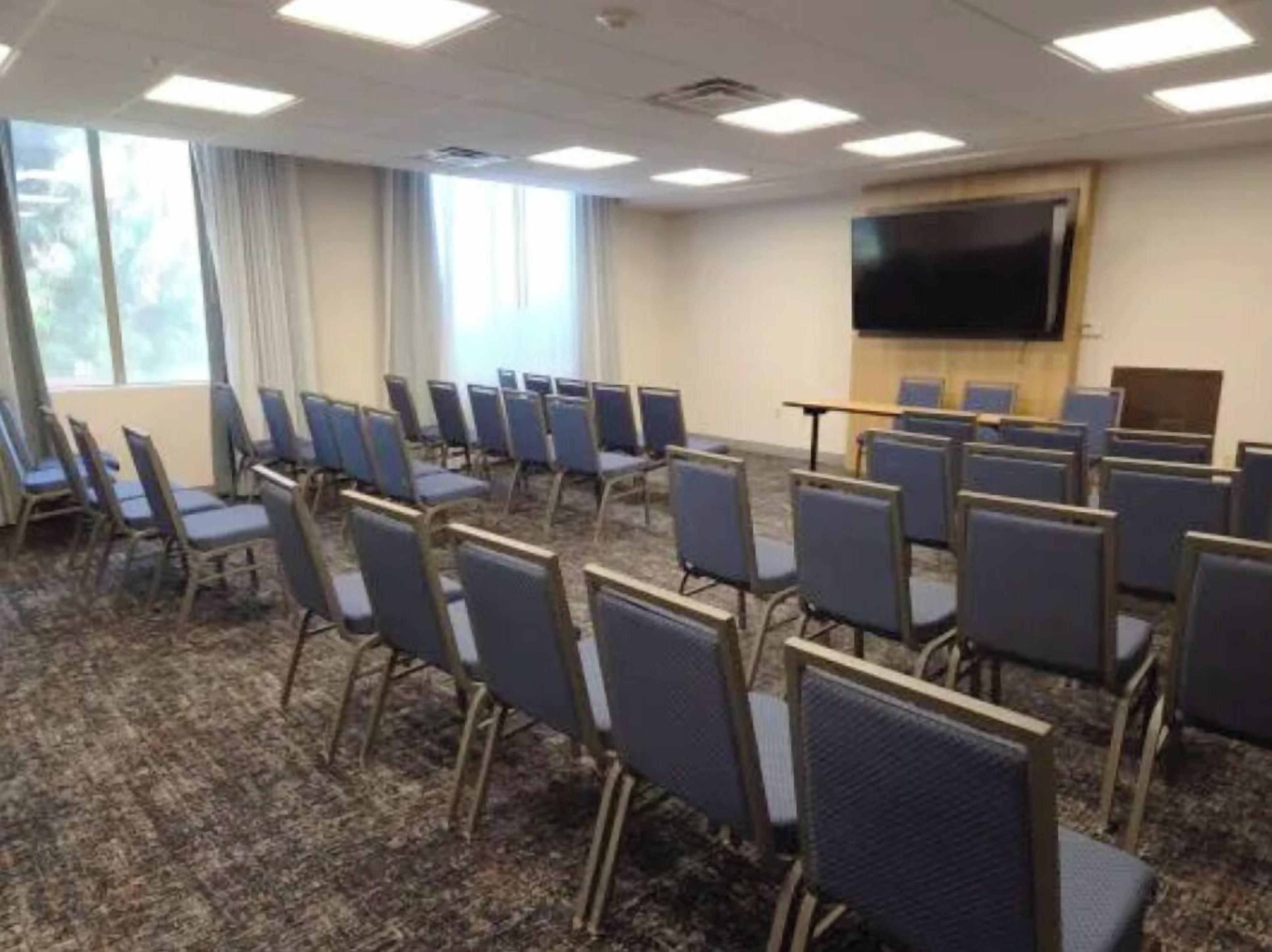 Ein Konferenzraum mit Reihen von Stühlen, einer großen Leinwand und einem Teppichboden.