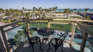 A balcony with a glass railing overlooking a beach, palm trees, and a parking area.