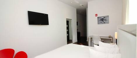 A hotel room with a bed, a desk, a chair, and a TV on the wall.