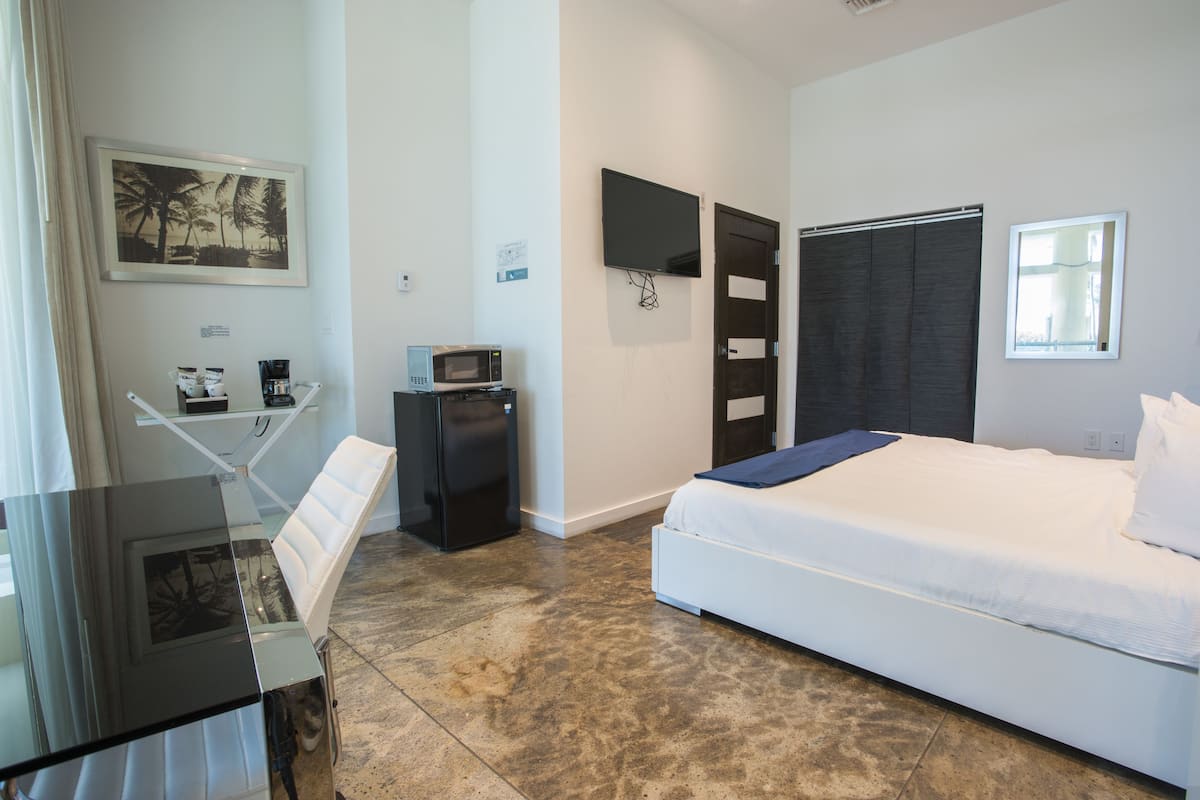 Una habitación de hotel con una cama, un escritorio con computadora, un microondas y un televisor en la pared.