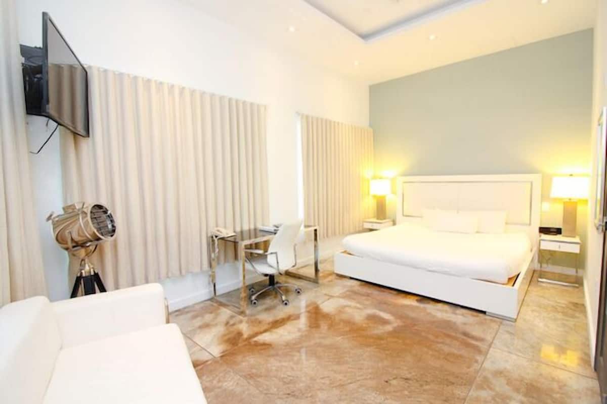 Una habitación de hotel con una cama grande, un escritorio con silla, un televisor montado en la pared y dos lámparas de noche.