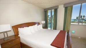 A hotel room with a large bed, a nightstand, a lamp, and a view of the beach.
