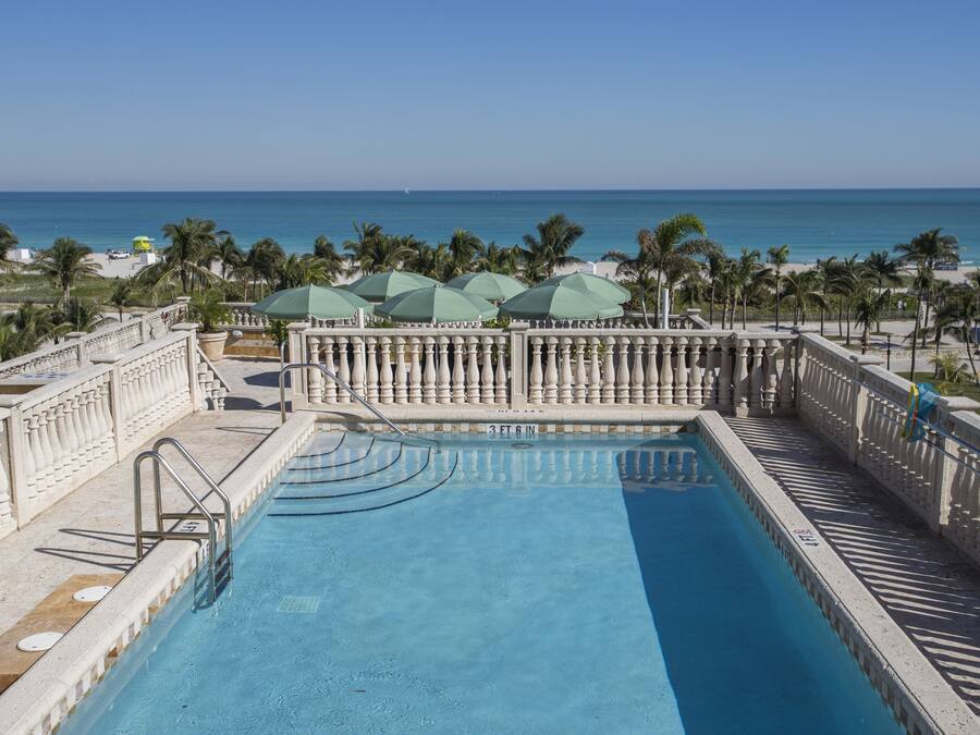 Una piscina con vista al océano, rodeada de palmeras y una barandilla.