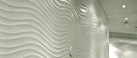 Un mur à texture avec un motif ondulé, un sol recouvert de moquette et un éclairage encastré.